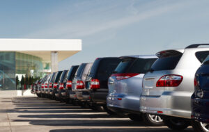 A line of vehicles in an auto lot outside a dealership.