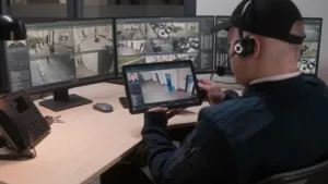 Security officer in headset controls and monitors CCTV cameras in coworking office, uses digital tablet and computers with playback on screens. High tech software showing surveillance cameras footage.