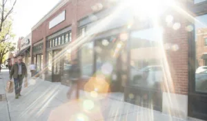 Busy street lined with storefronts, sunlight bouncing off large windows and creating a bright glare